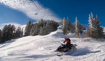 a person riding a snowmobile down a snow covered slope at Aspen Suite - Hot Tub, Minutes to RMNP, Walking Distance to Mary's Lake in Estes Park