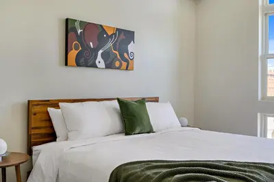 a bedroom with a bed with white sheets and green pillows at Canvas & Comfort | Espadin LoHi in Denver