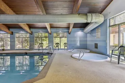 a swimming pool with two hot tubs in a room with windows at Winter Park Condo with Resort Shuttle On-Site! in Winter Park
