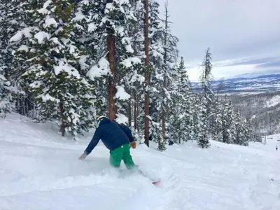 a person on a snowboard in the snow near trees at Wagon Wheel at Rendezvous home in Fraser