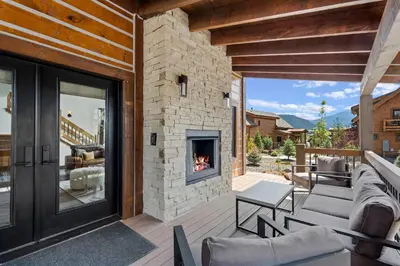 a patio with a stone fireplace on a house at Cabin on Lake Estes! Private Jacuzzi Two Patios Indoor and Outdoor Fireplace in Estes Park