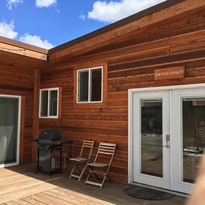 a wooden cabin with chairs and a table on a deck at Native Spirit Cabin at Base Camp in Dumont