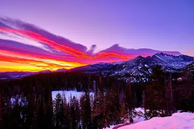 a sunset over a mountain range with trees and a lake at Little Matterhorn 17A Condo in Estes Park
