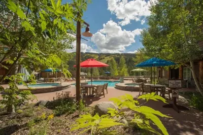 a patio with tables and umbrellas and a swimming pool at Cozy And Quaint 1 Bedroom Condo In The Heart Of River Run Village in Keystone