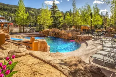 a pool in a backyard with chairs and rocks at Beautiful 2 Bedroom Mountain Condo In River Run Village With Hot Tub Access And Walking Distance To The Gondola in Keystone