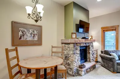 a living room with a table and a stone fireplace at Expedition Station Condos by Vail Resorts in Keystone
